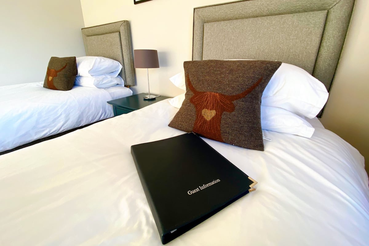 A hotel room with two beds, each with a headboard, a nightstand with a lamp, and a black folder labeled "Guest Information".