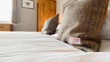 Een keurig opgemaakt bed met een Harris Tweed kussen en een ingelijste foto van een koe aan de muur.