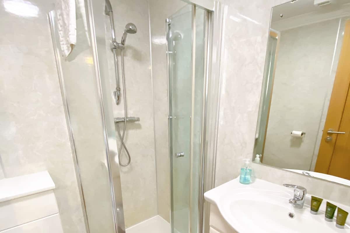 A modern bathroom with a glass-enclosed shower, a white toilet, a sink with toiletries, and a mirror.