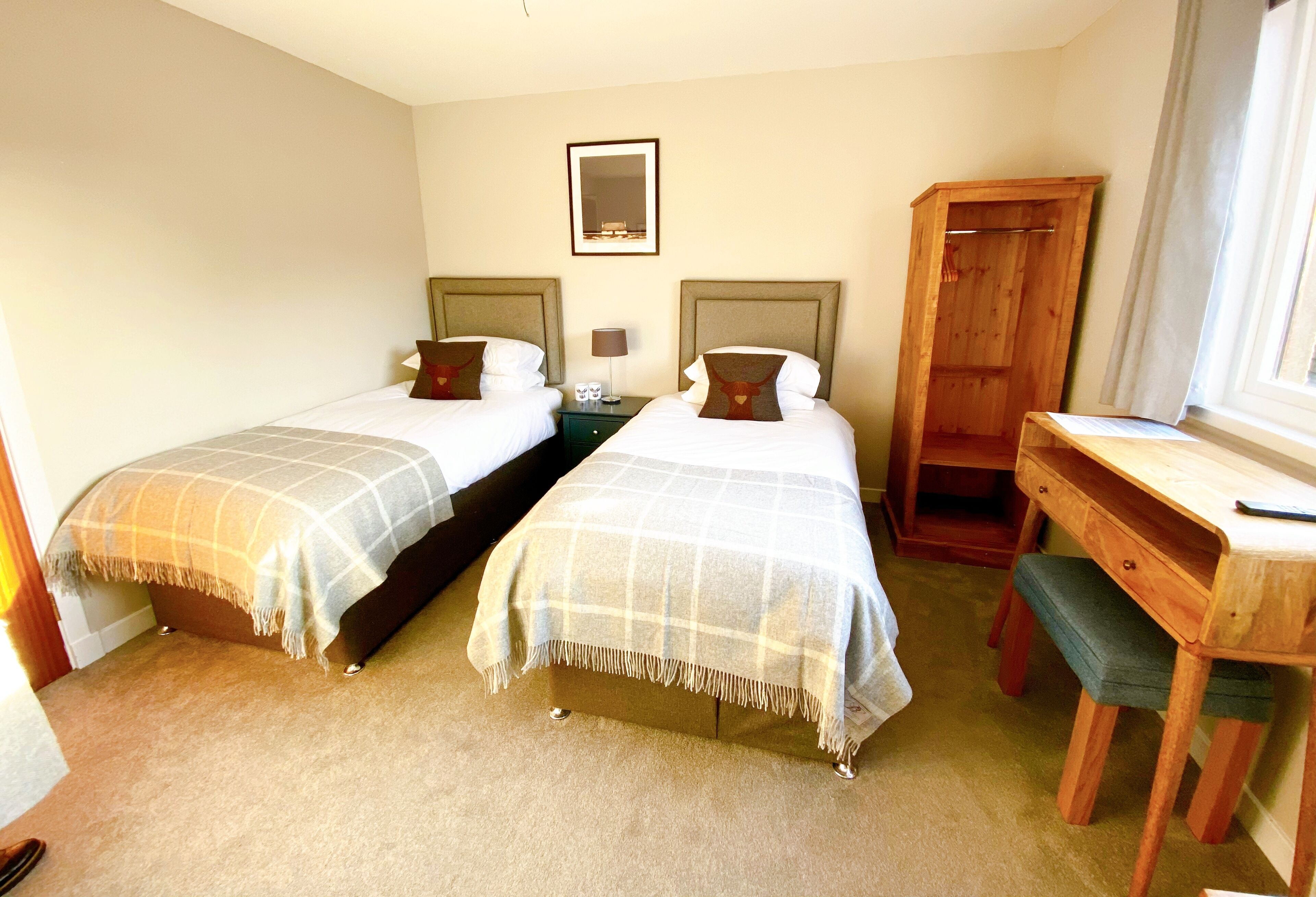 A hotel room with two beds, a wooden desk, a mirror, and a window.