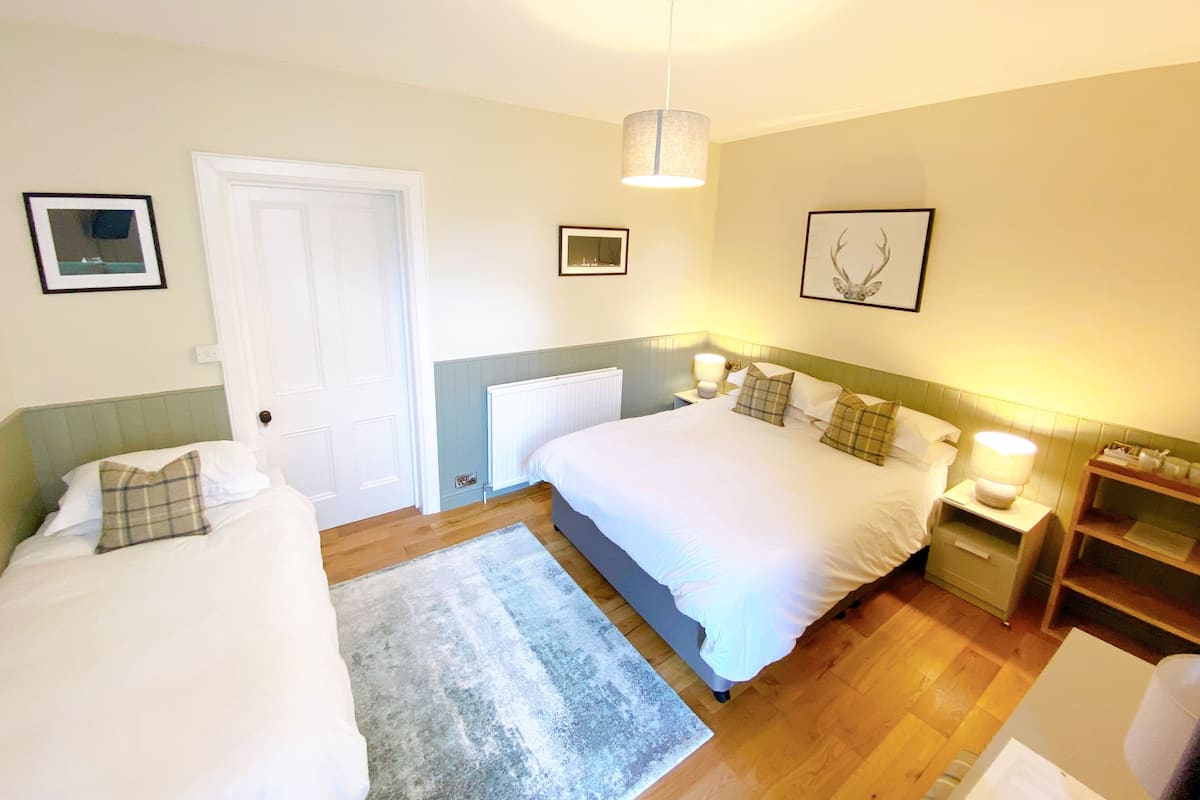 A bedroom with two beds, a wooden floor, a white door, and framed pictures on the walls.
