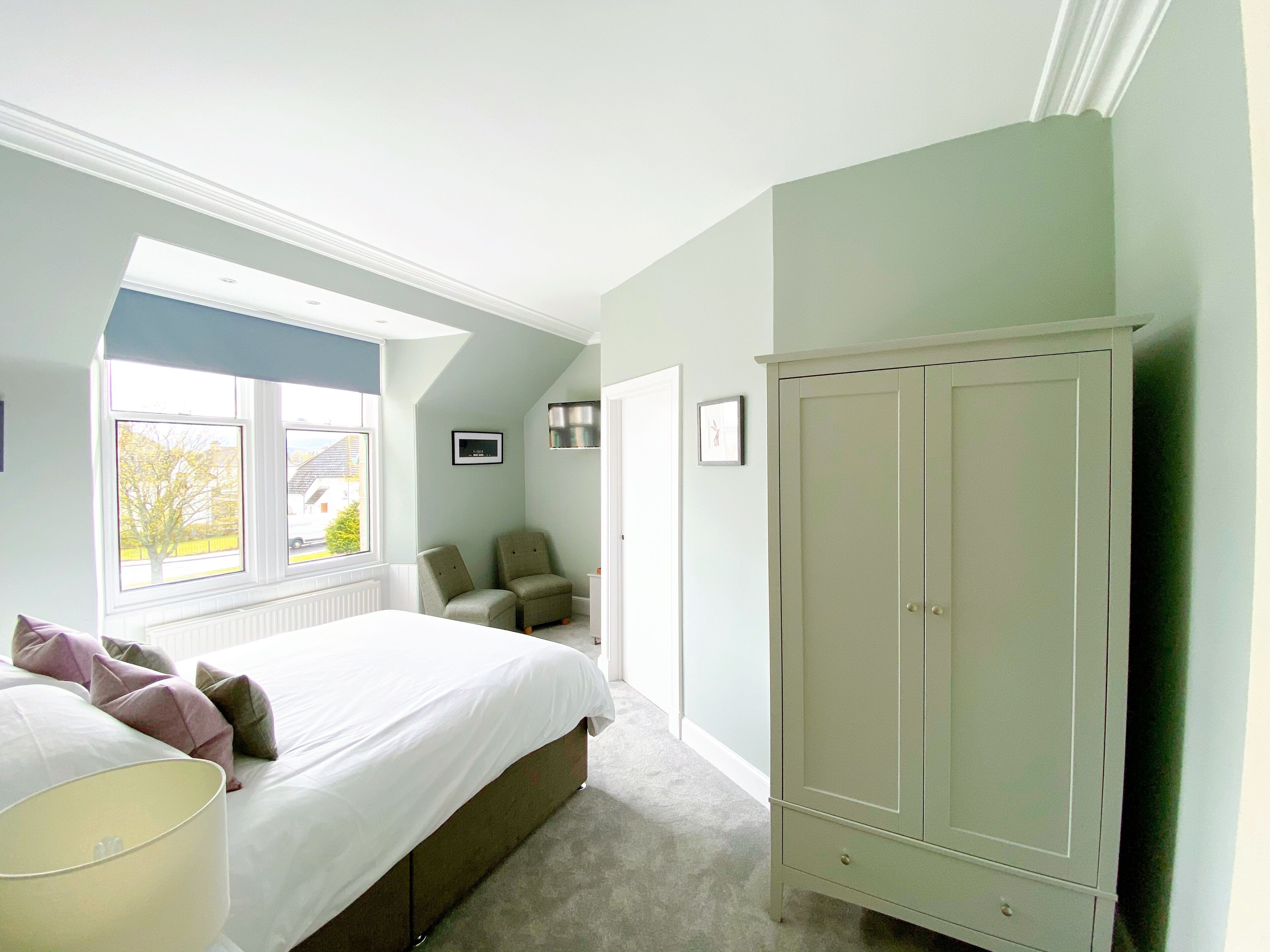 A bedroom with a bed, a wardrobe, a chair, and a window with a view of the outside.