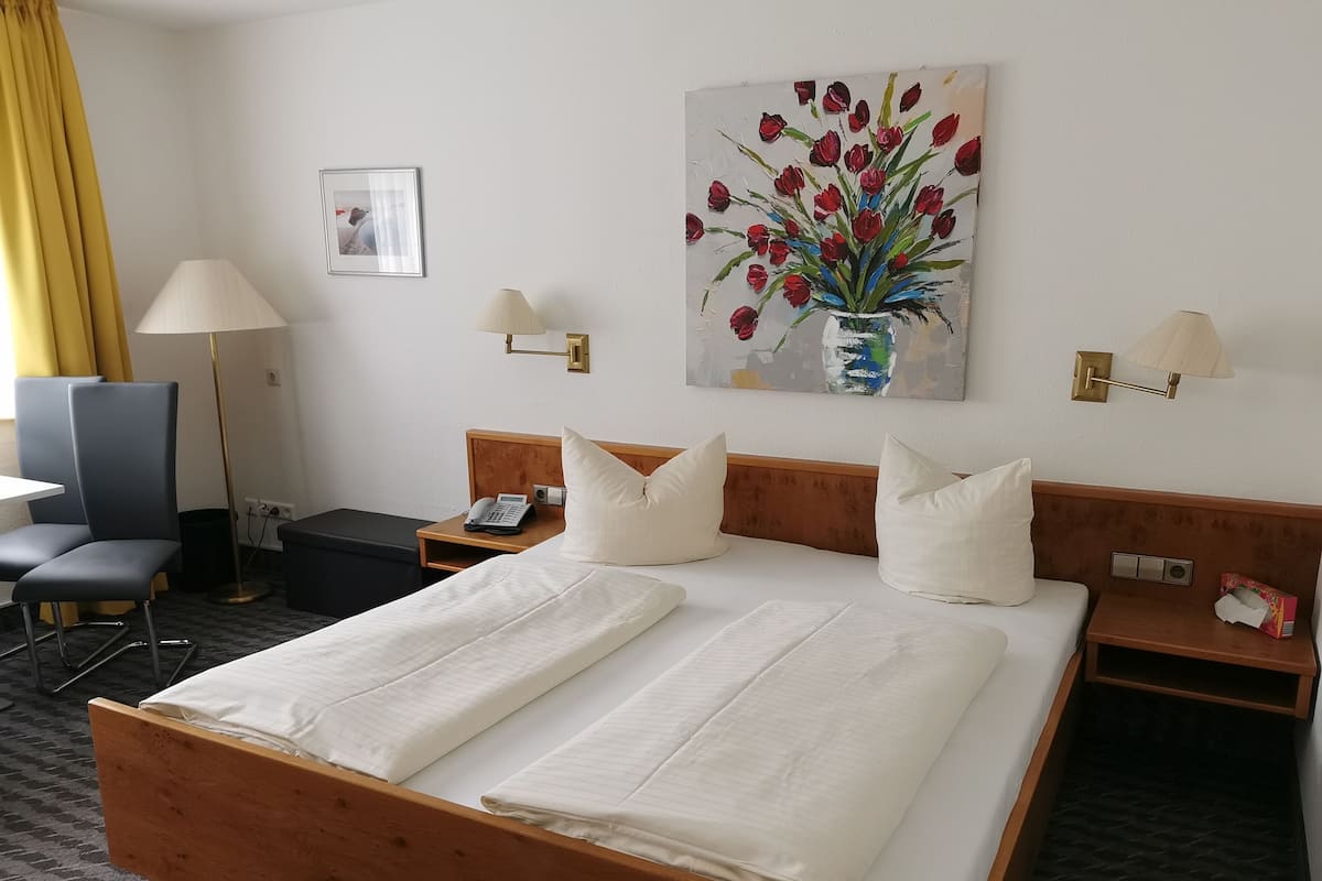 Ett hotellrum med en säng i trä, två sängbord, ett skrivbord, en stol, en lampa och en tavla med röda tulpaner.