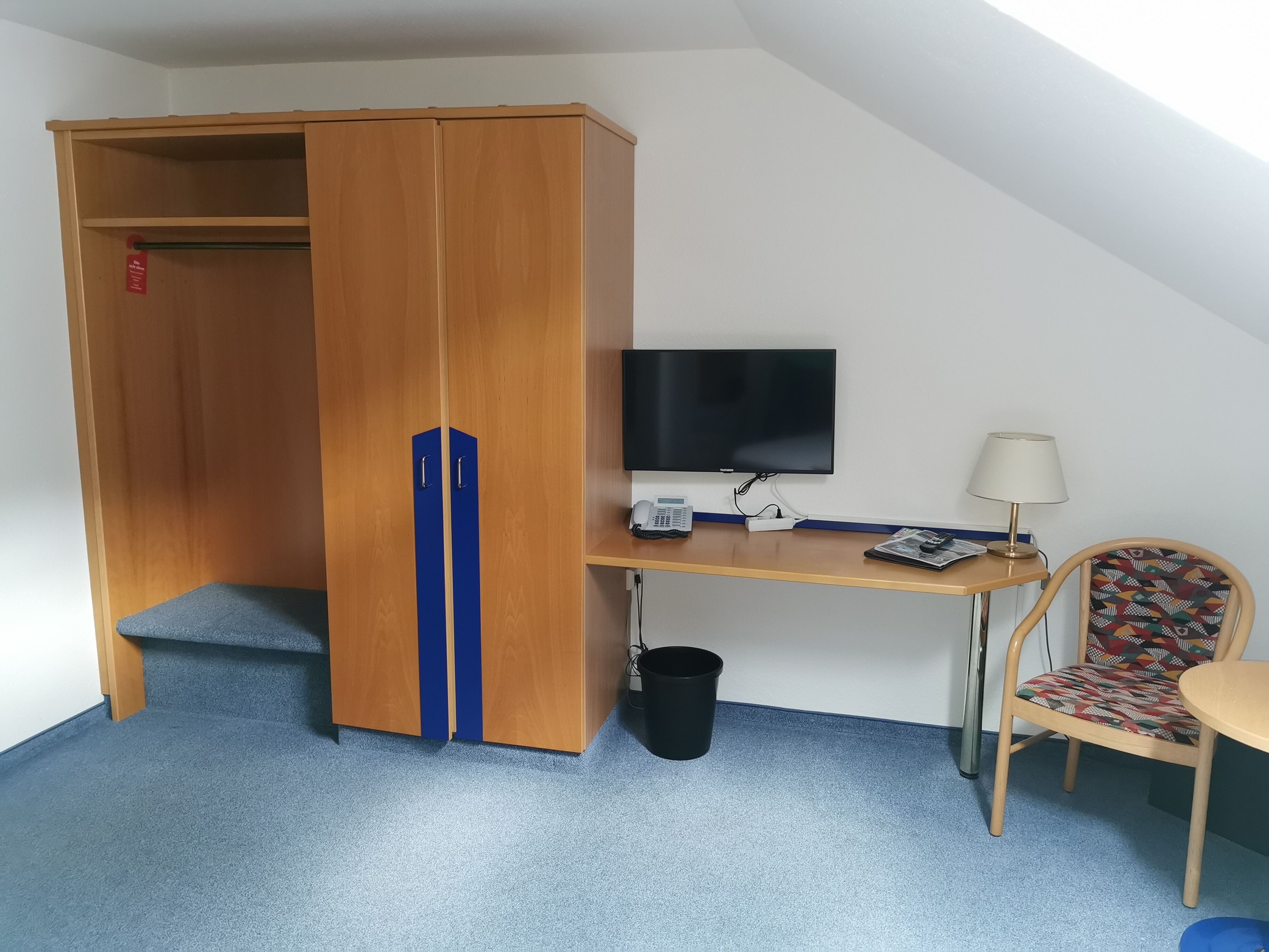 Una habitación pequeña con un armario de madera, un escritorio con computadora, una silla y un televisor.