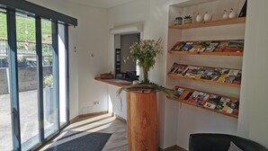 Zona de recepción con un escritorio de madera, una planta en maceta y una estantería de pared con revistas.