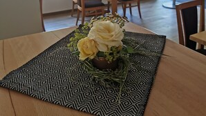 Un área de comedor con una mesa dispuesta para dos personas, destacando un mantel individual estampado y un centro de mesa floral.