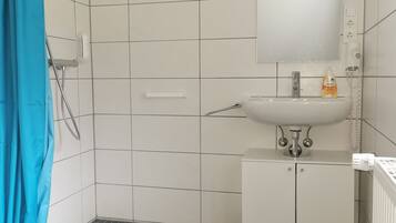 Un baño con ducha, lavamanos y espejo.