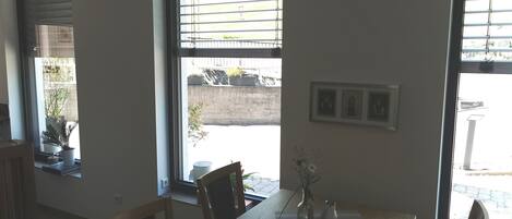 A room with a wooden table, chairs, a window with blinds, and a wall-mounted picture frame.