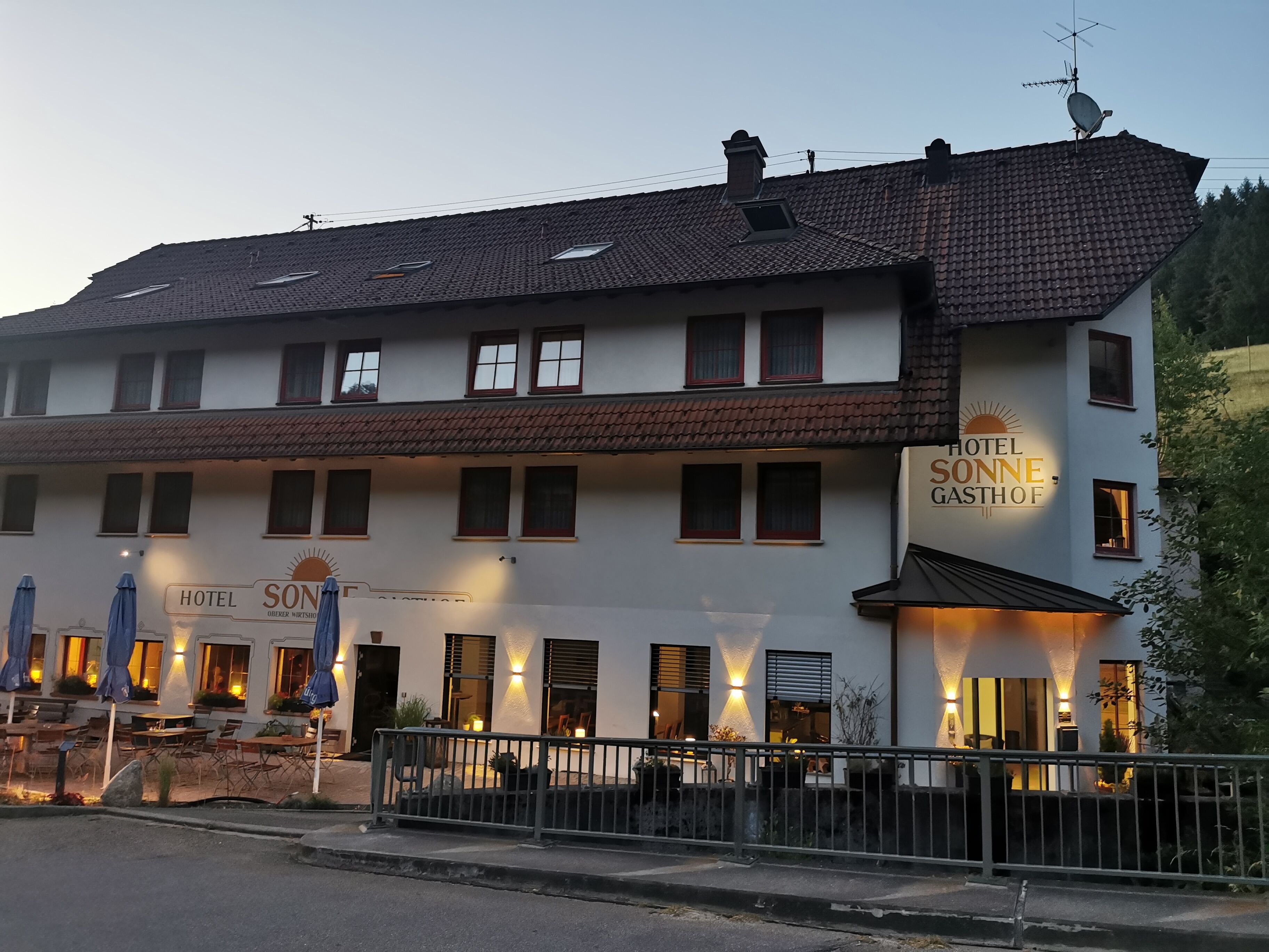 Een hotel met een witte gevel, meerdere ramen en terras met parasols.