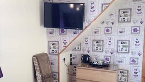 A room with a TV mounted on the wall, a patterned chair, a wooden dresser, and a trash can. - Dunroamin (Aviemore)