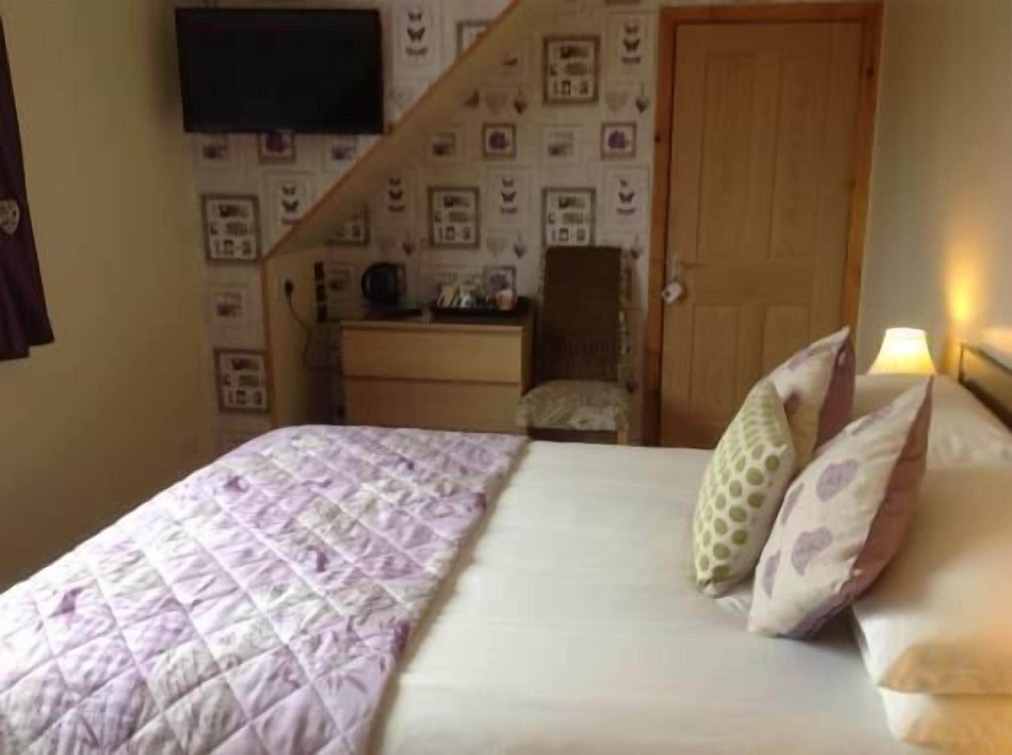 A bedroom with a bed, pillows, a dresser, a television mounted on the wall, and a door.
