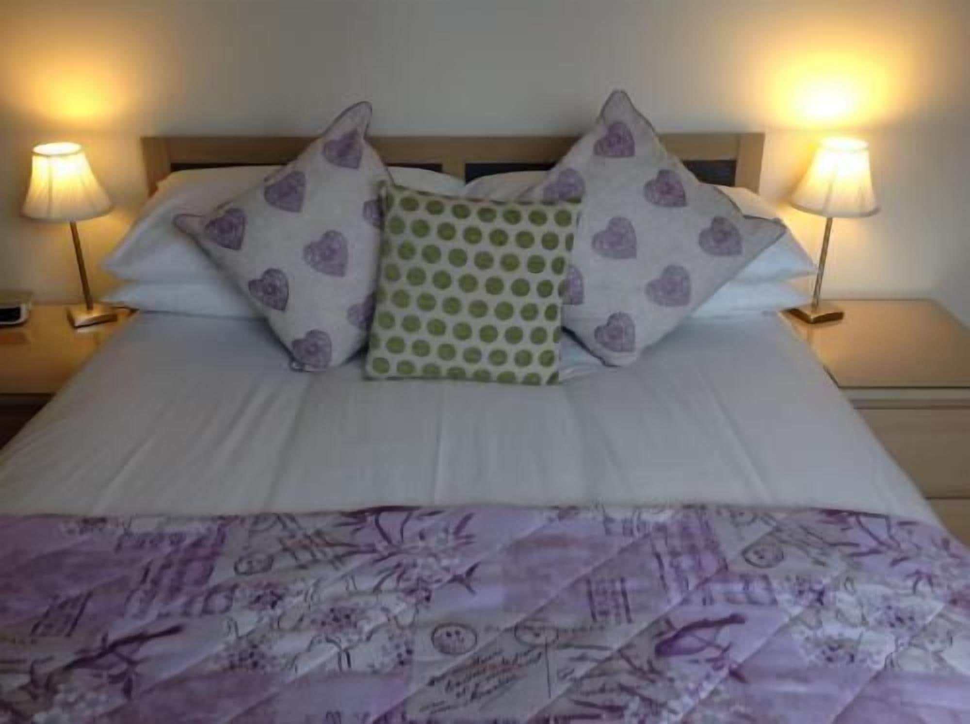Un lit bien fait, recouvert d’une couvre-lit à motifs, avec deux coussins décorés de motifs en forme de cœur et deux lampes de chevet.
