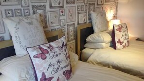 A bedroom with two beds, each with white bedding and decorative pillows. - Dunroamin (Aviemore)