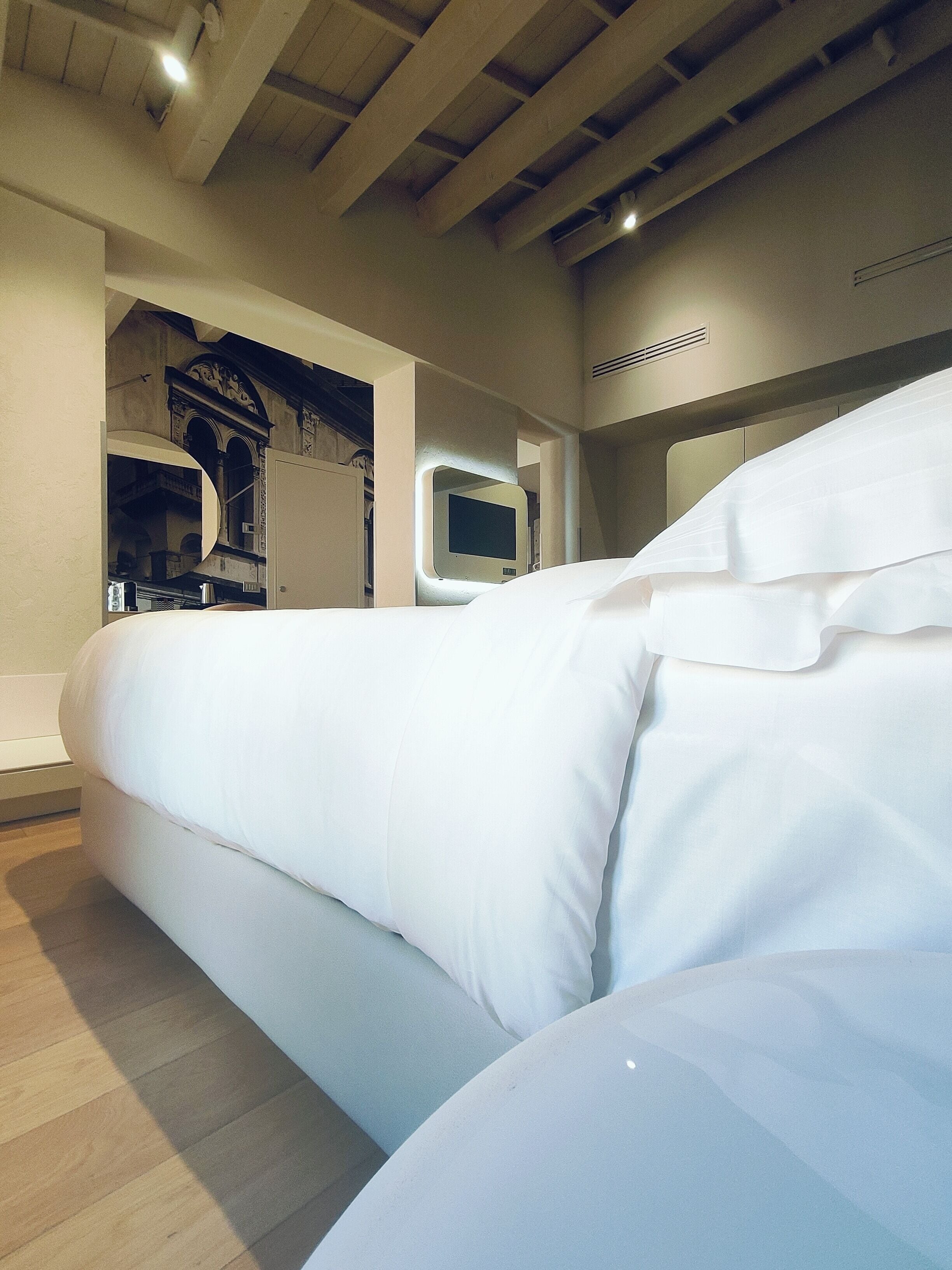 A modern hotel room with a large bed, a built-in TV, and a wooden ceiling.
