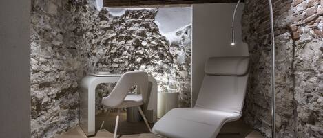 Une salle de spa avec un mur en pierre, un fauteuil de massage, une petite table et un lampadaire.