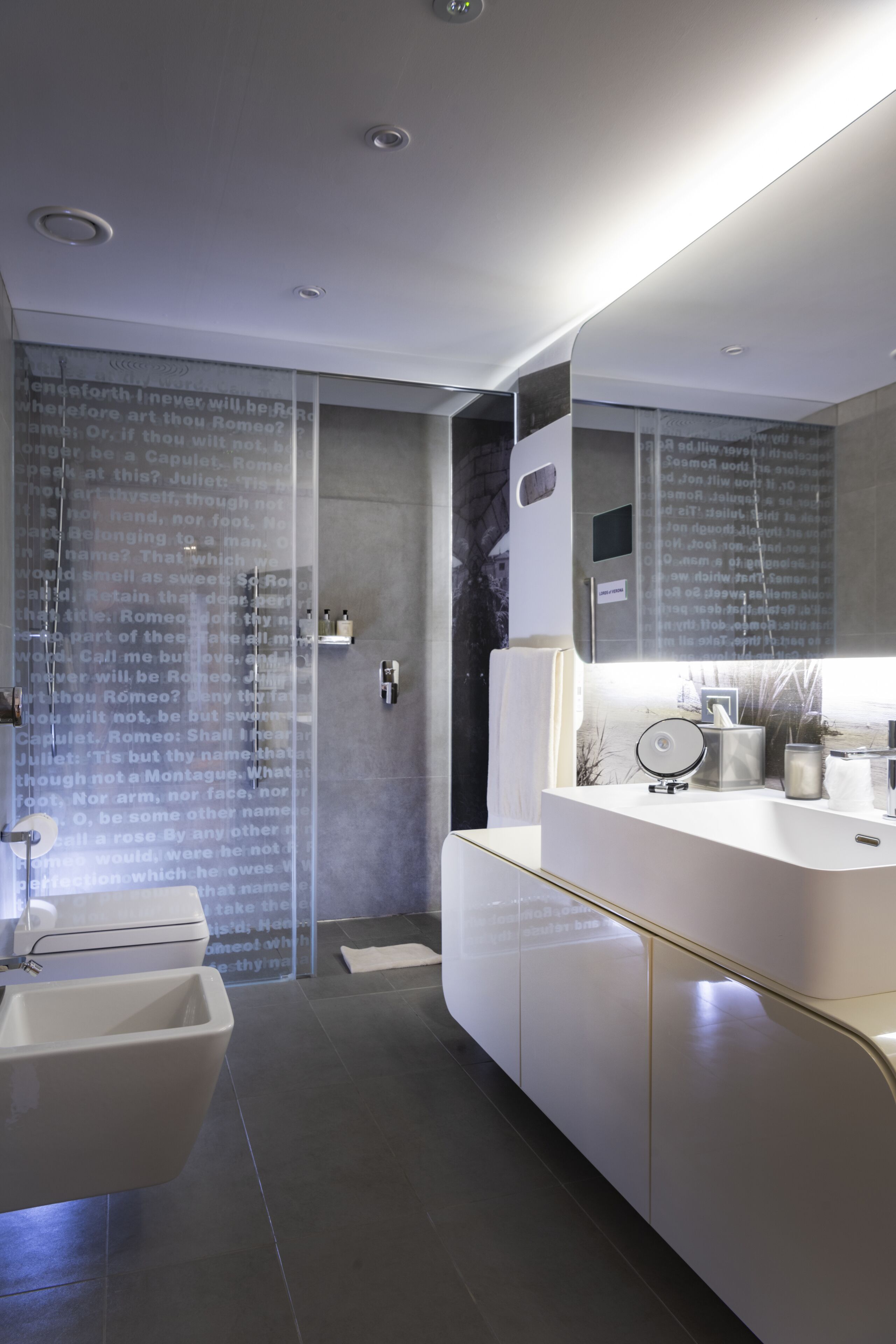 A modern bathroom with a glass shower enclosure, a white vanity with a mirror, and a large mirror above the vanity.
