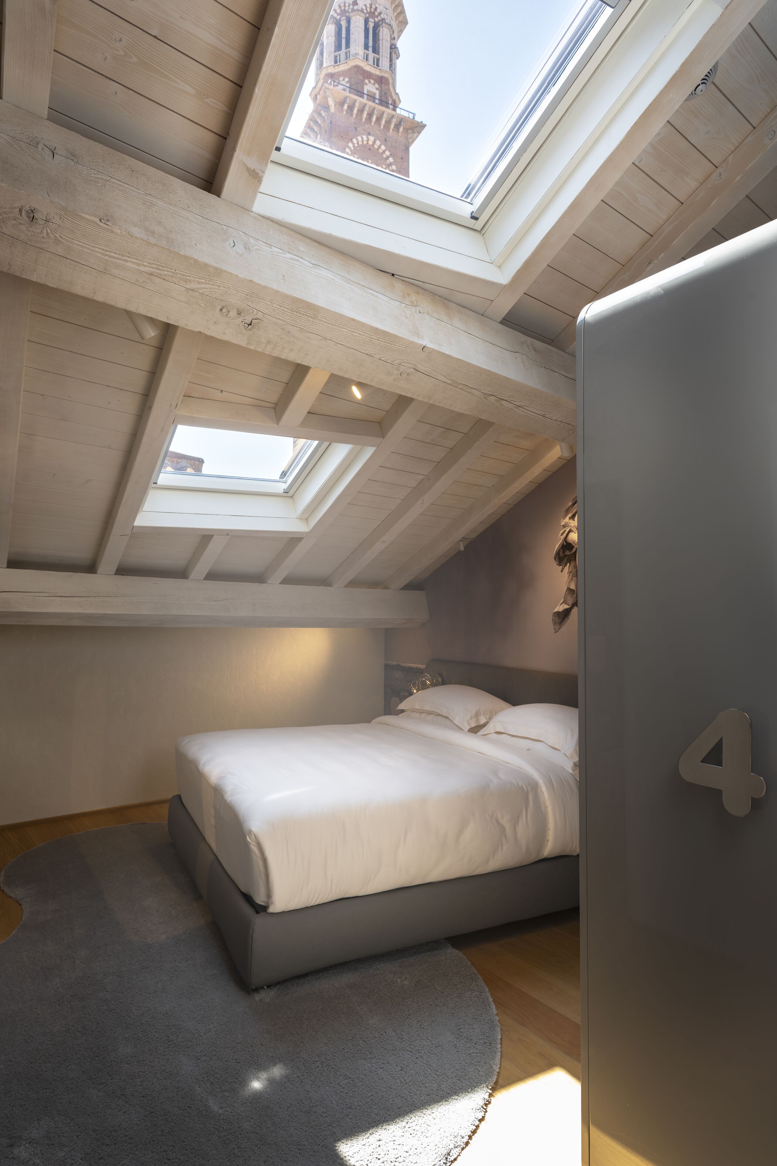 A bedroom with a skylight, a bed, a gray rug, and a wall-mounted number '4'.