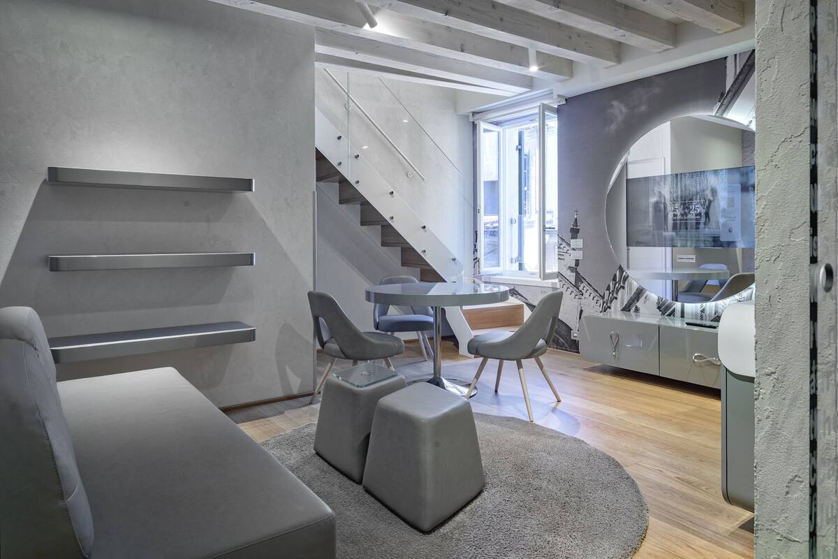 A modern living room with a staircase, grey furniture, and a large window.