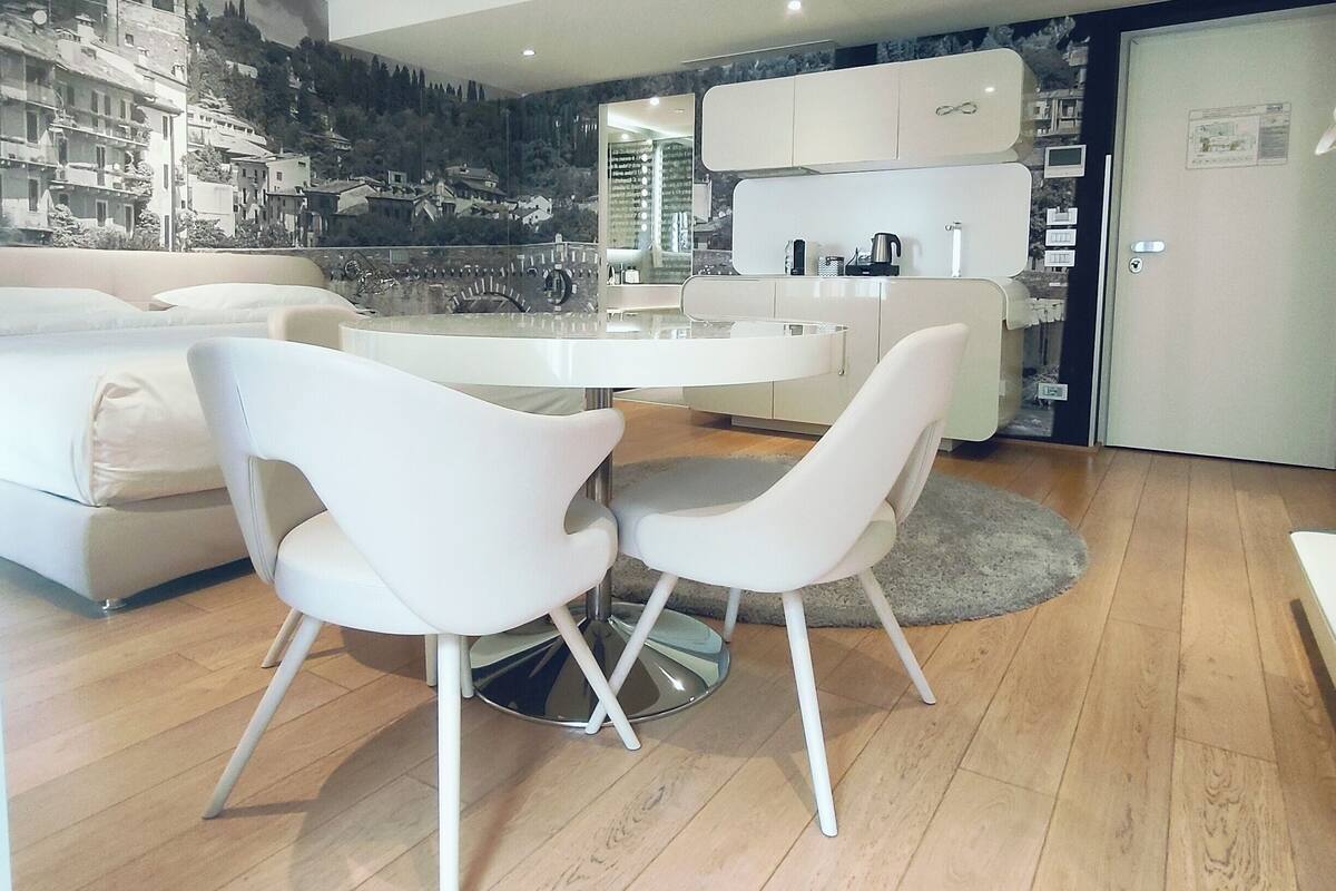 A modern living room with a dining area, featuring a white sofa, a dining table with two chairs, and a kitchen area with cabinets and a refrigerator.
