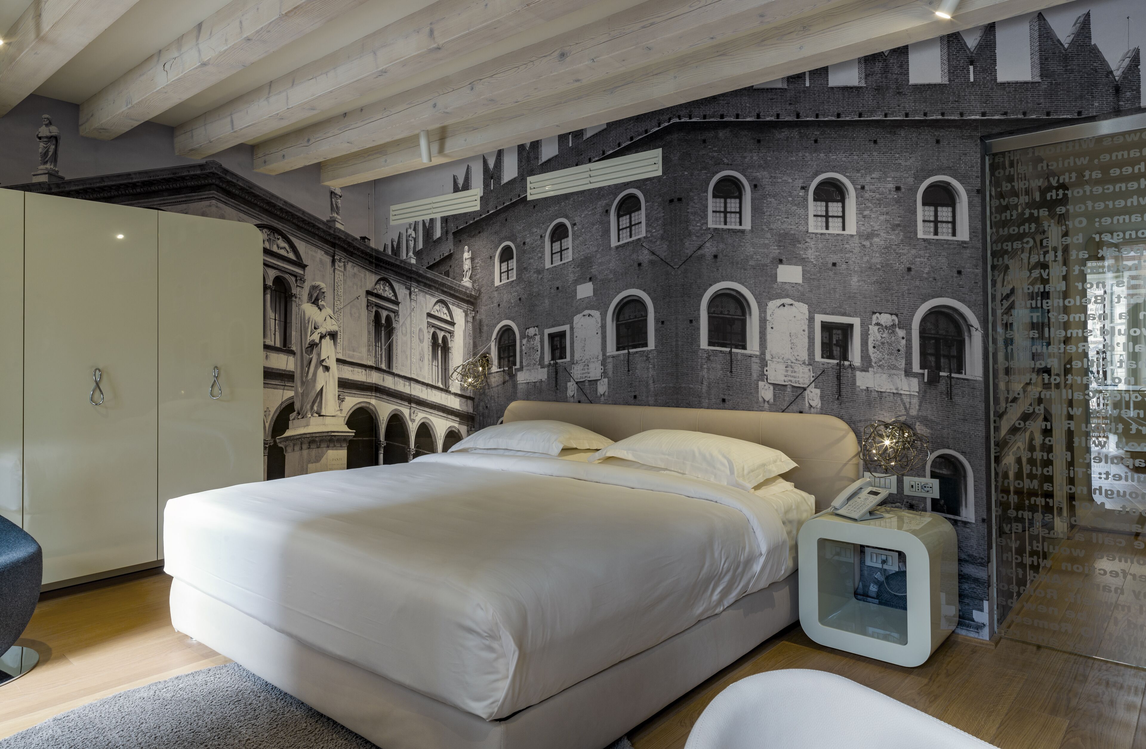 A bedroom with a large bed, a wardrobe, and a wall mural of a building facade.
