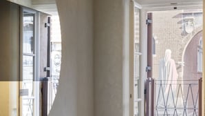 Une salle de bain moderne avec un grand miroir, un plancher en bois et une vue sur une statue, visible à travers une porte ouverte.
