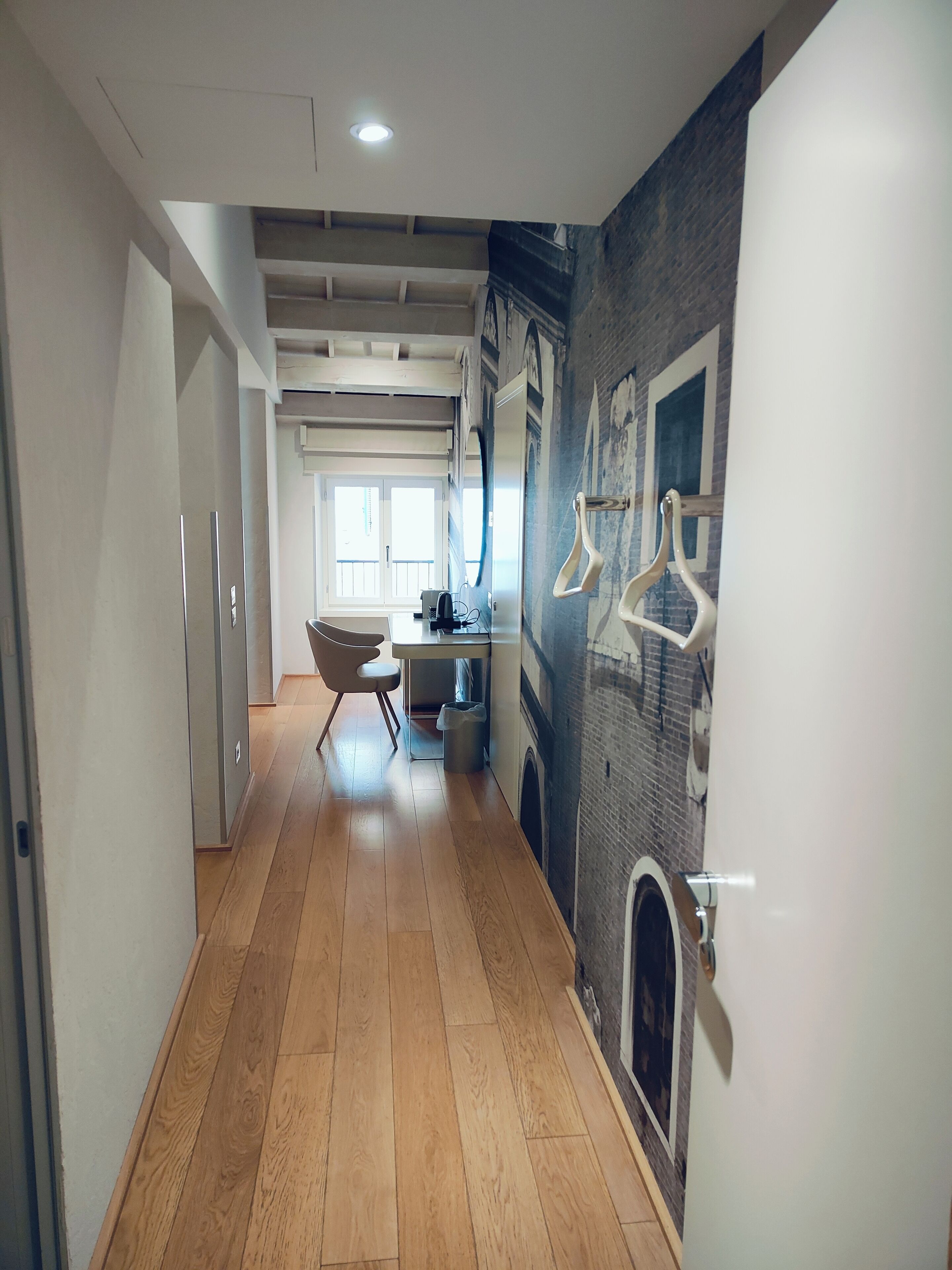 A modern kitchen with a built-in oven, a dining area with a chair, and a hallway with wooden flooring and a hanging coat rack.
