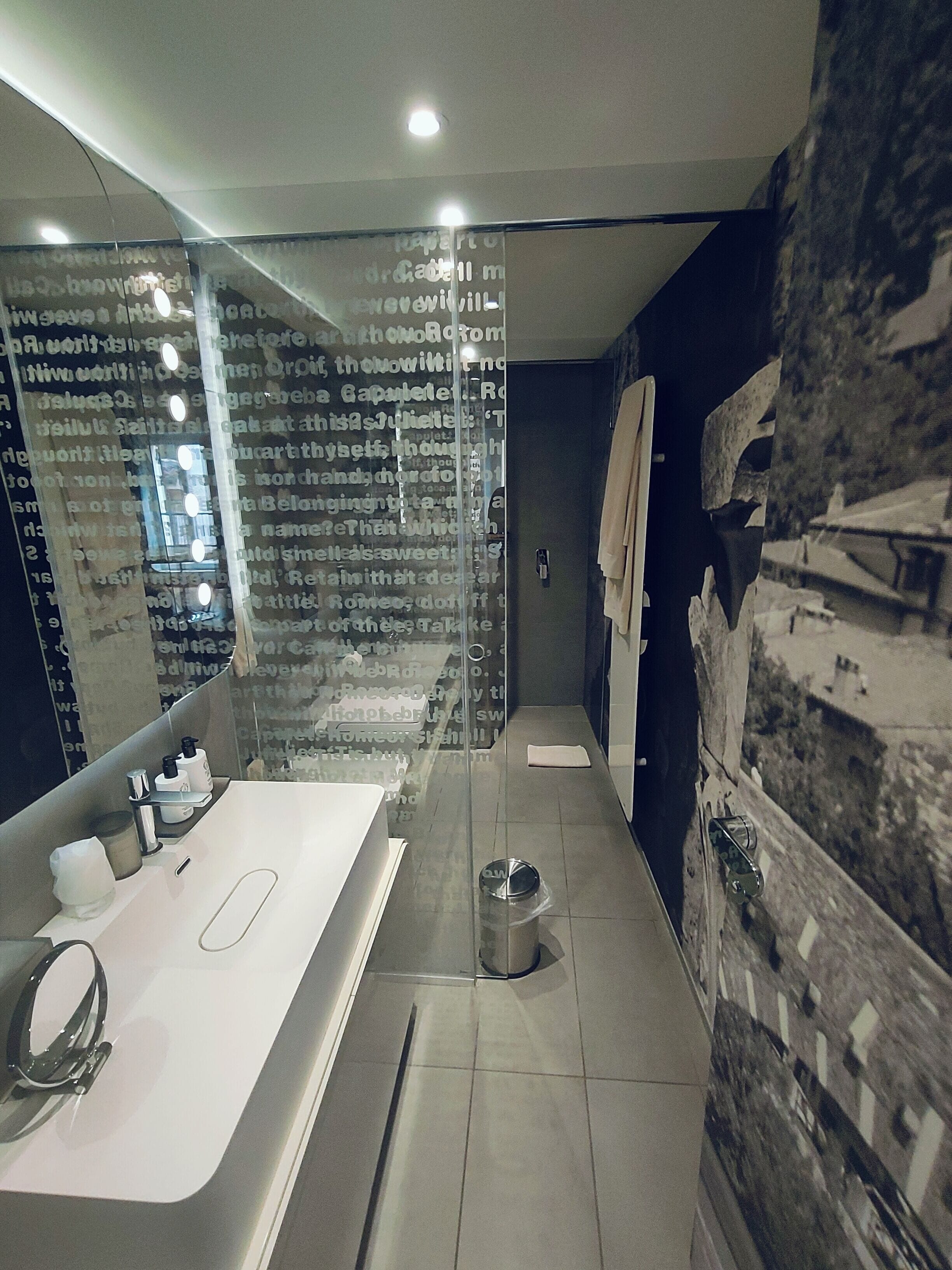 A modern bathroom with a large mirror, a white sink, and a glass shower enclosure.