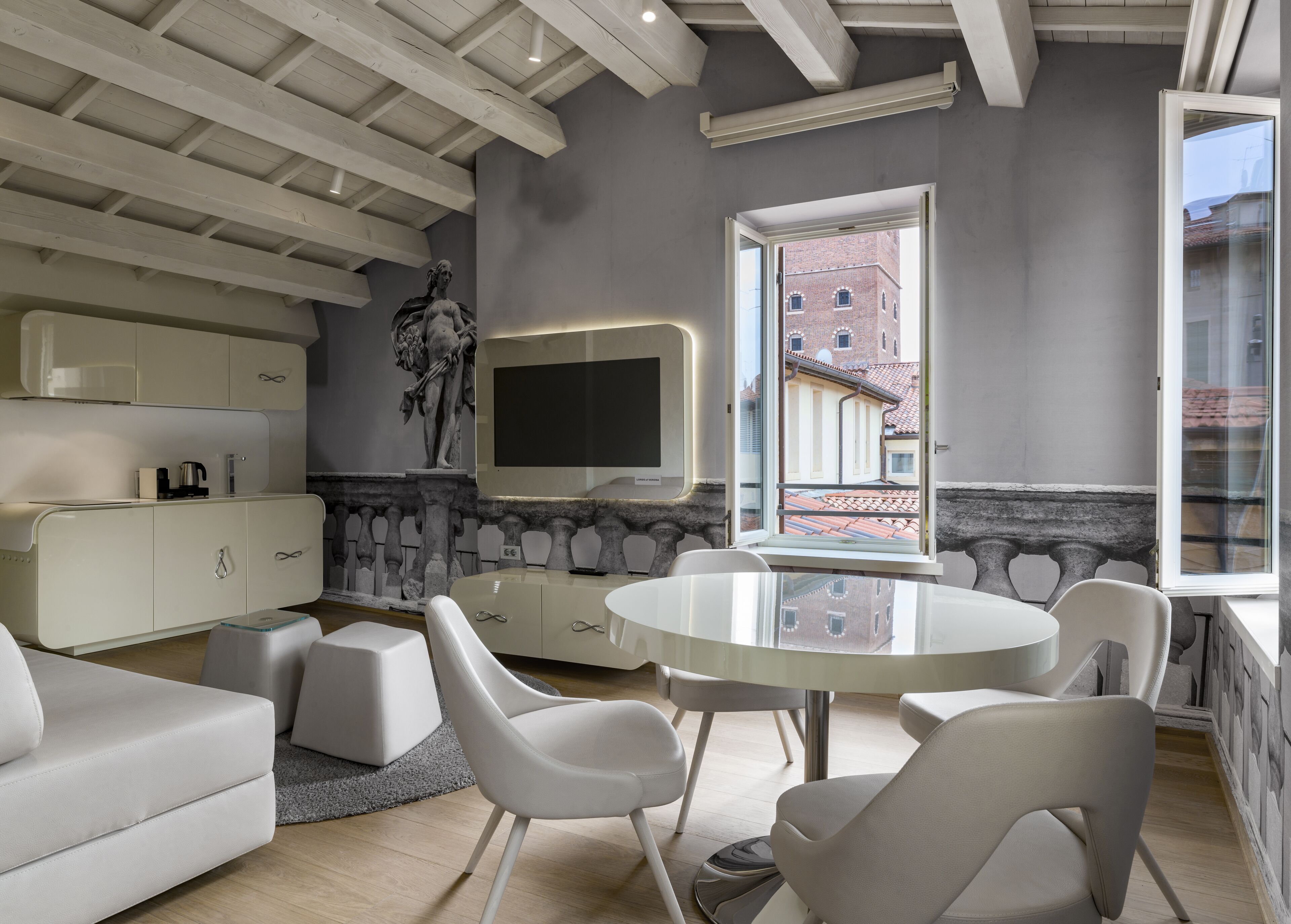 A modern living room with a round table, white sofas, a TV, and a view of a building through a window.
