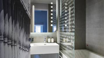 A modern bathroom with a large mirror, a sink with two bottles, a shower with a glass door, and a decorative wall with text.