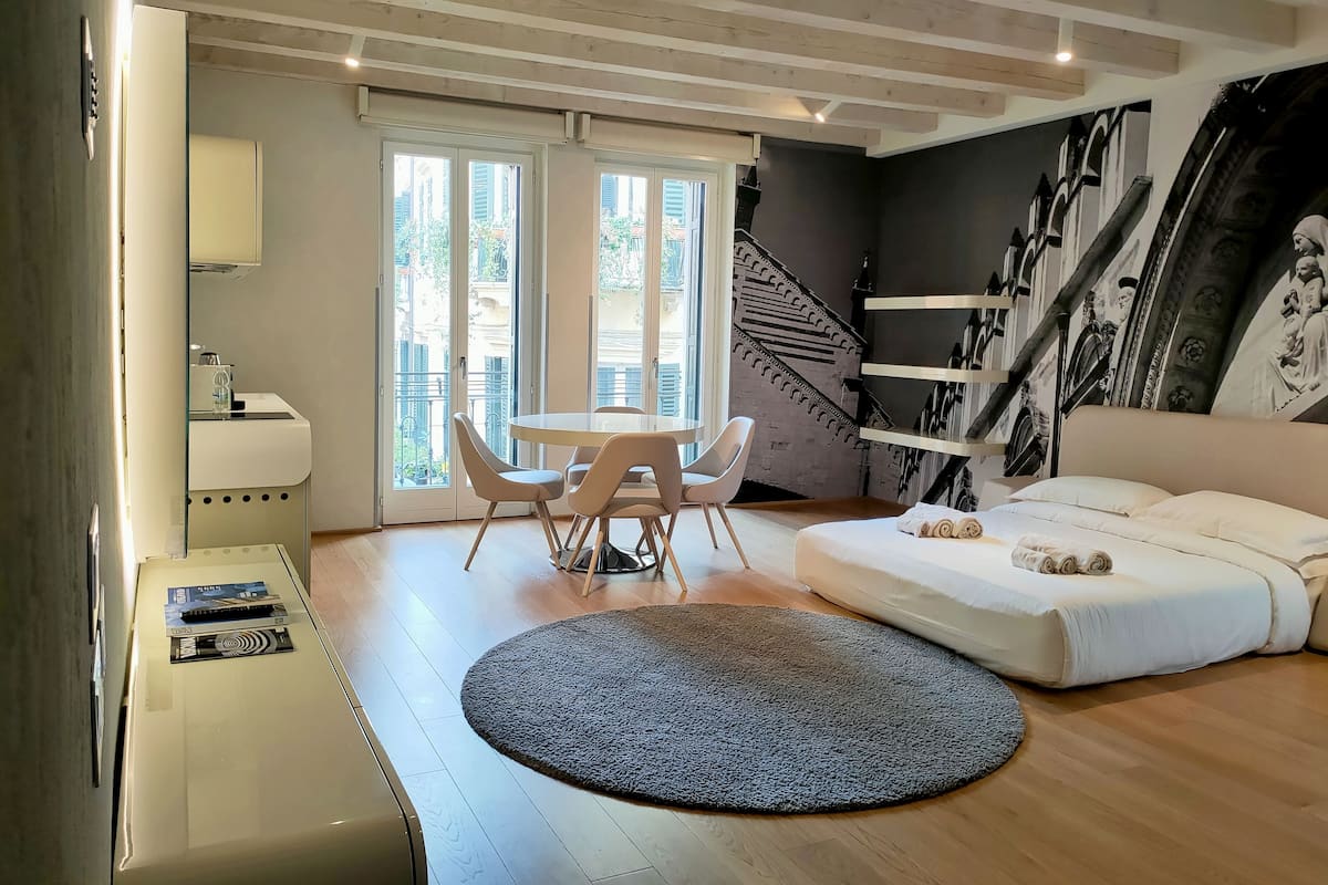 A modern living room with a round table, two chairs, a sofa, a large rug, and a staircase with a mural.