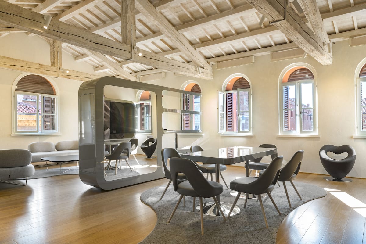 A spacious room with a high wooden ceiling, a large mirror, and a dining area with modern chairs and a table.