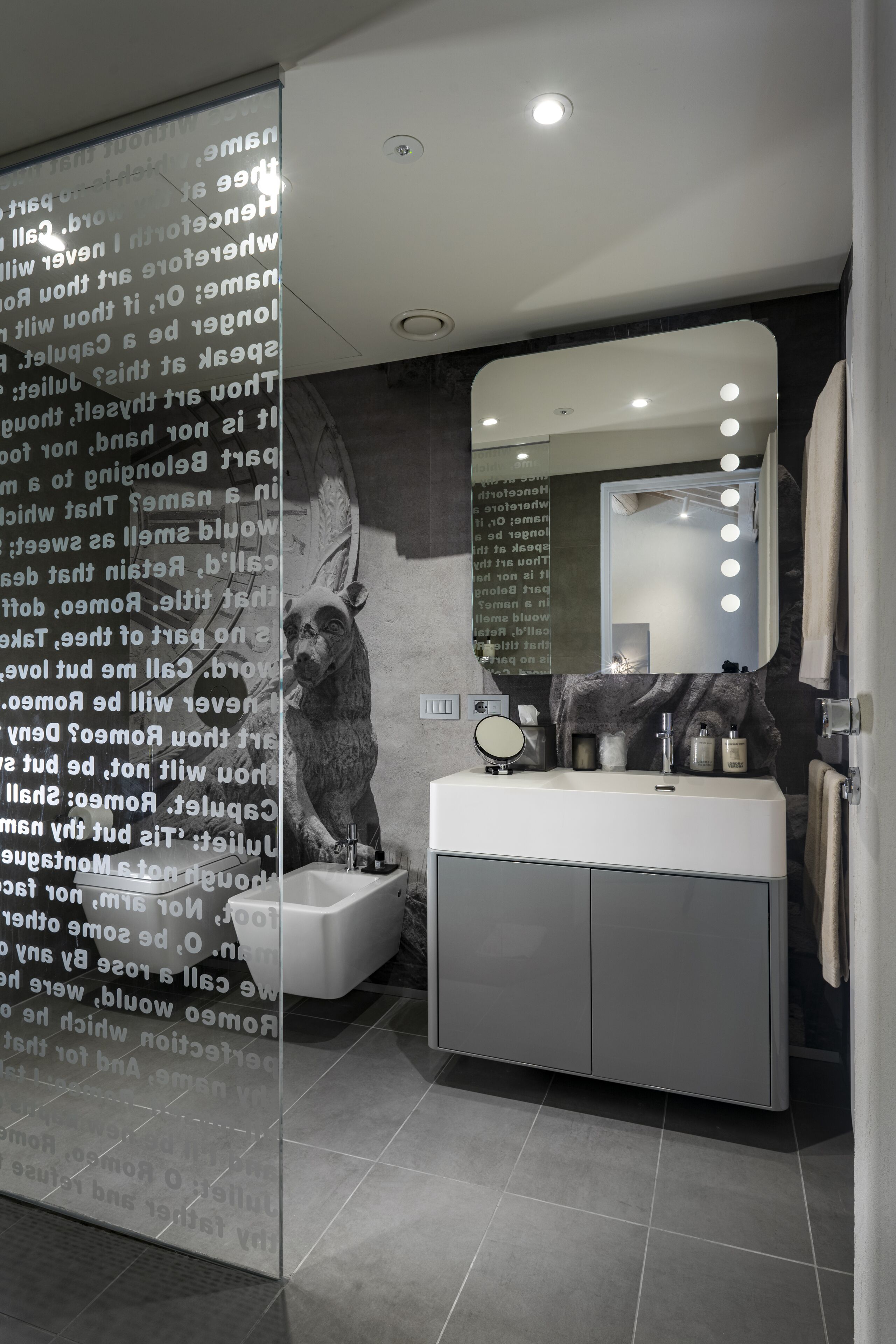 Une salle de bain moderne avec un grand miroir, un meuble-lavabo et un luminaire fixé au mur.