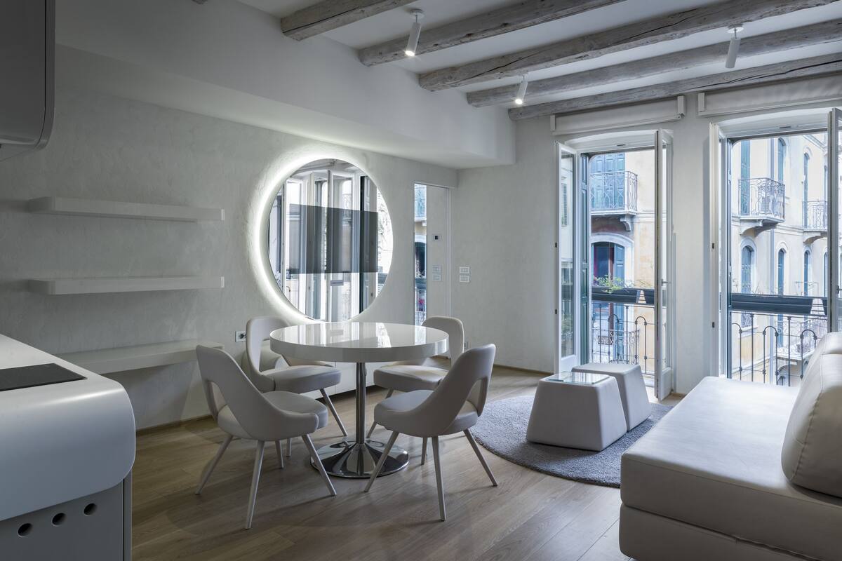 A modern interior with a round table, white chairs, and a large circular mirror.