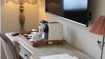 A wooden desk with a lamp, a coffee maker, a remote control, and a tray with a cup and a glass.