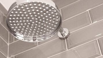 Um chuveiro com design redondo e perfurado, fixado numa parede com azulejos retangulares.