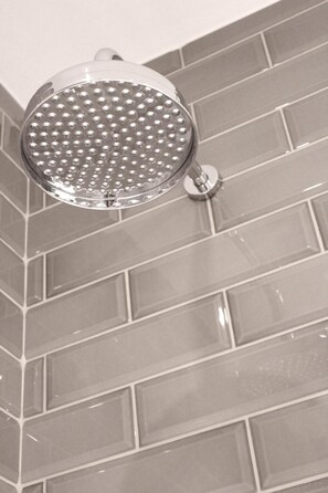 A showerhead with a round, perforated design, mounted on a wall with rectangular tiles. - The Grafton Arms Pub & Rooms (London)