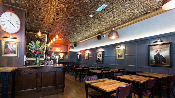 Un interno ristorante con tavoli e sedie in legno, un soffitto decorativo e quadri appesi alle pareti.