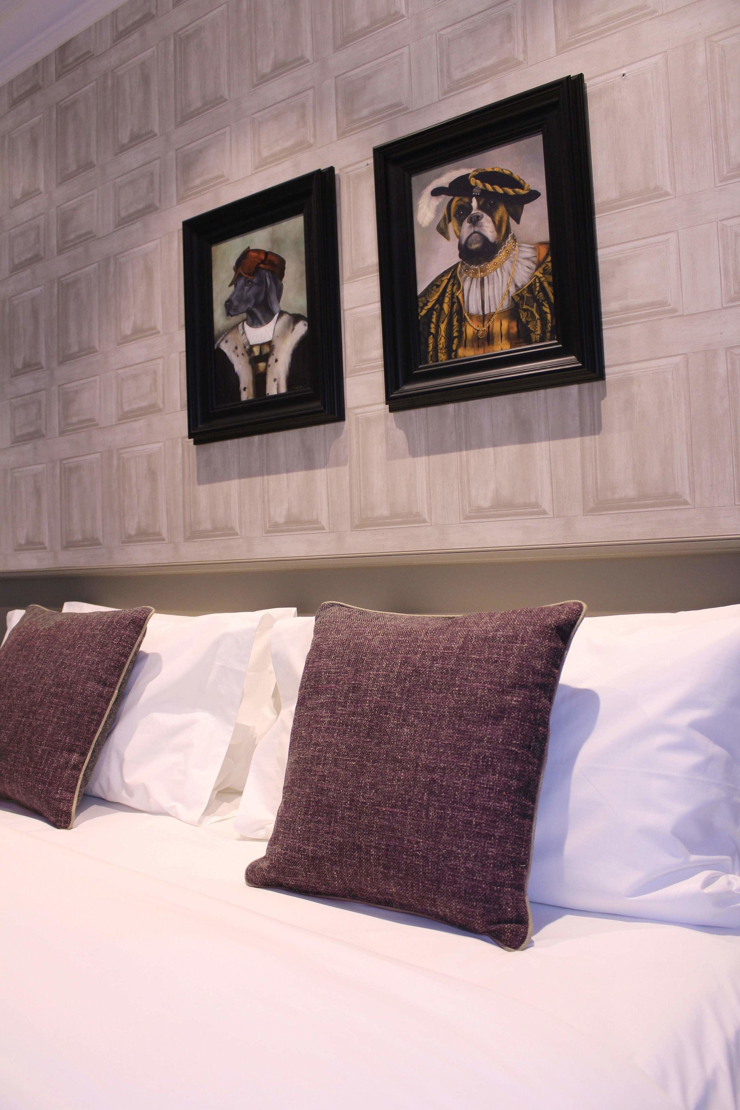 Une chambre d’hôtel avec un lit, des oreillers blancs et violets, et deux tableaux encadrés accrochés au mur.