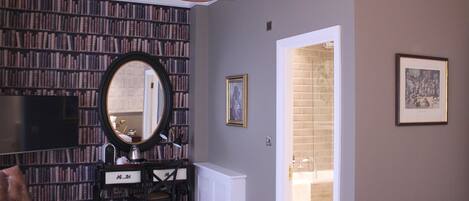 A room with a bookshelf, a desk with a mirror, a leather chair, and a chandelier.