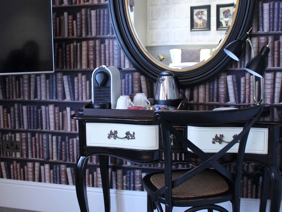 A room with a desk, chair, and a large mirror. There are bookshelves in the background.
