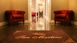 A hotel hallway with two red armchairs on either side, a polished floor, and a carpet with 'Villa San Martino' written on it. - Villa San Martino (Naples)