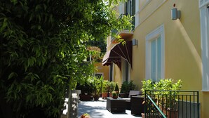 A narrow alleyway with potted plants and outdoor furniture, leading to a building with a yellow facade and a green railing. - Villa San Martino (Naples)