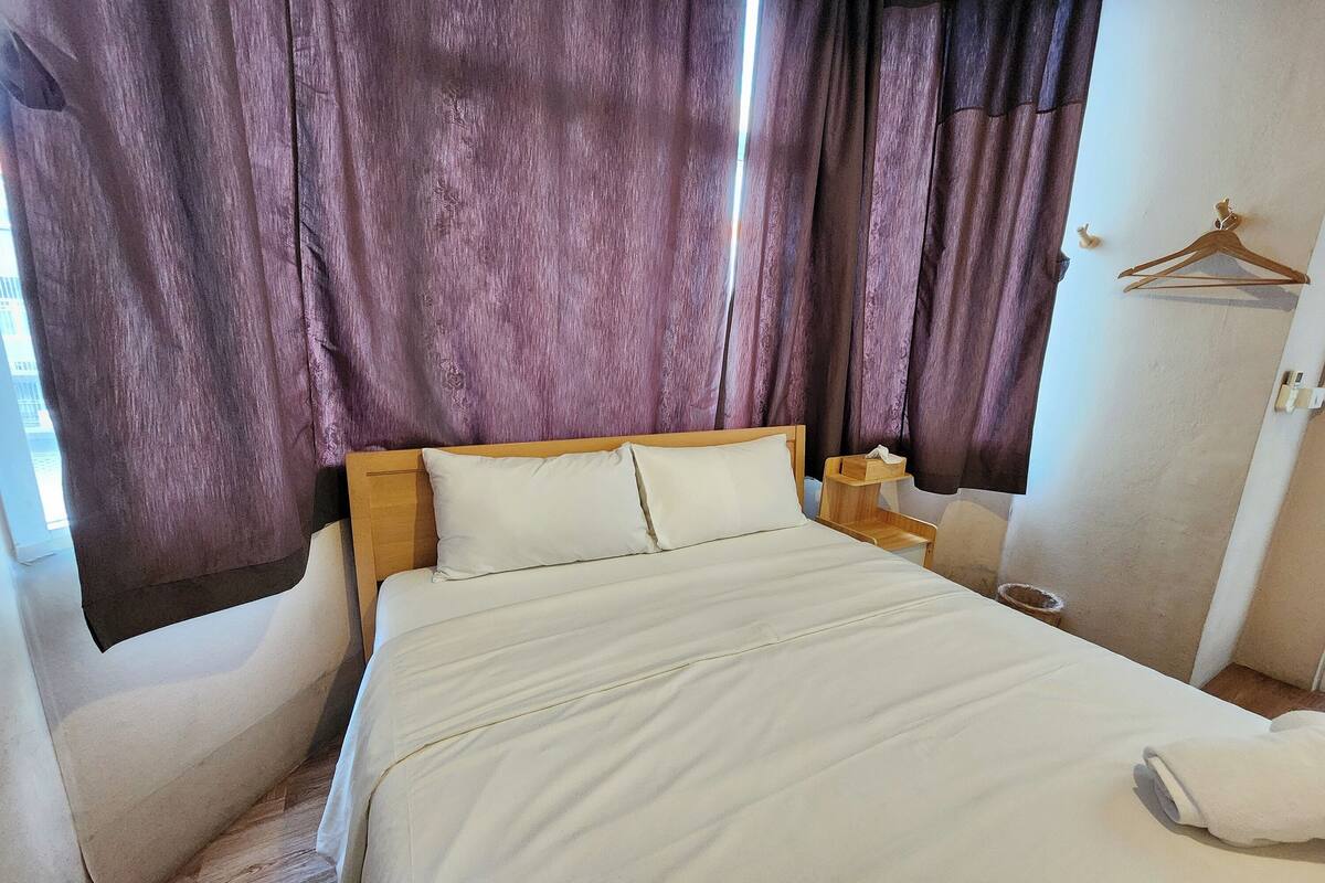 A neatly made bed with white linens, a wooden headboard, and a wooden nightstand with a lamp.