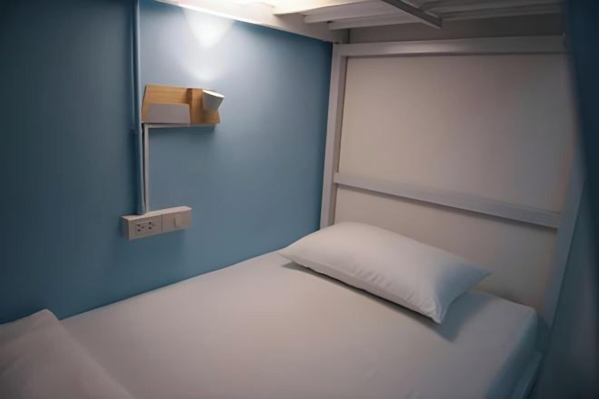 Una cama individual con ropa blanca en una habitación con paredes azules y una ventana.
