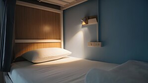 A neatly made bed with white linens, a wooden headboard, and a wall-mounted light fixture. - Ease Hostel (Bangkok)