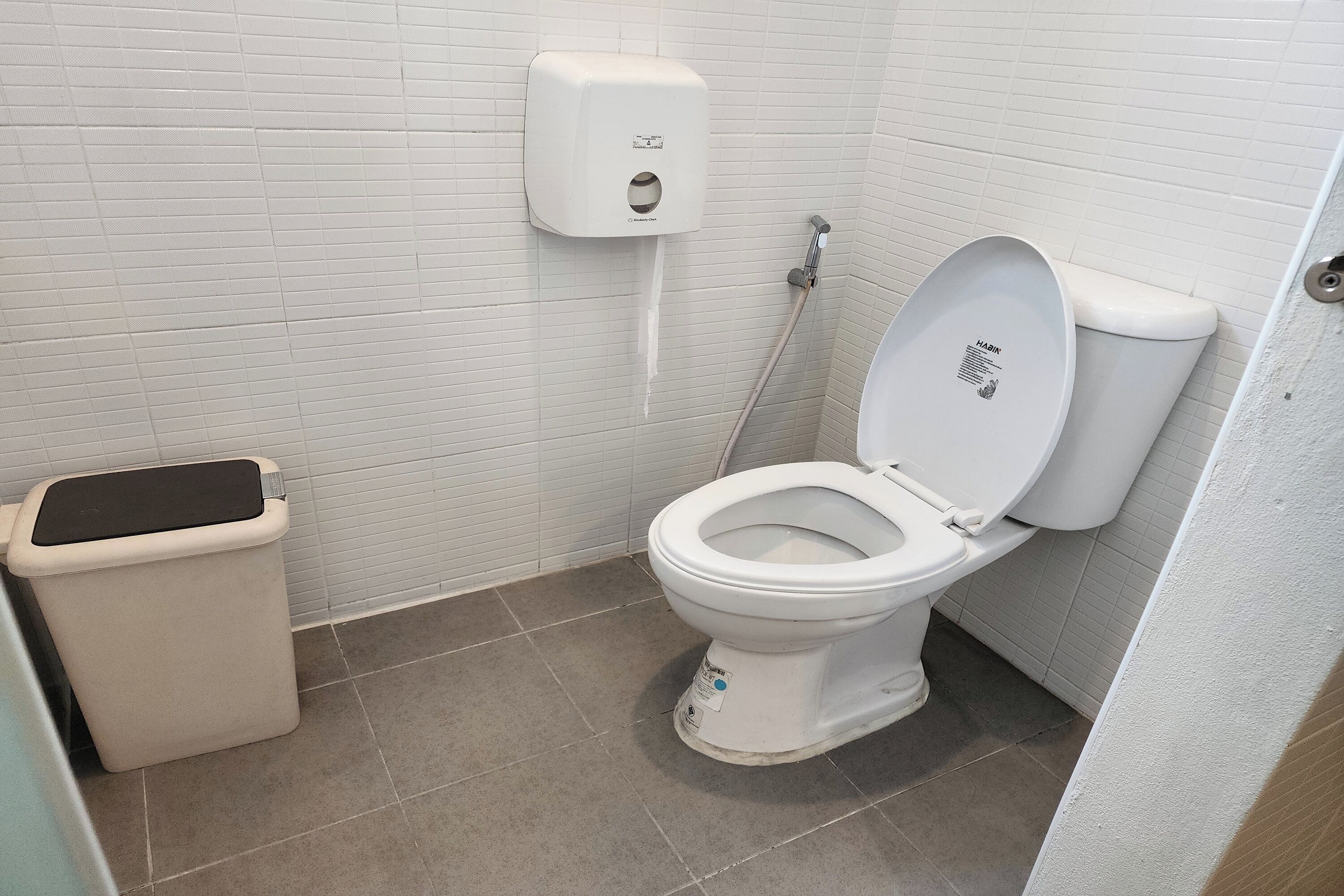 A standard bathroom with a toilet, a trash bin, and a soap dispenser.