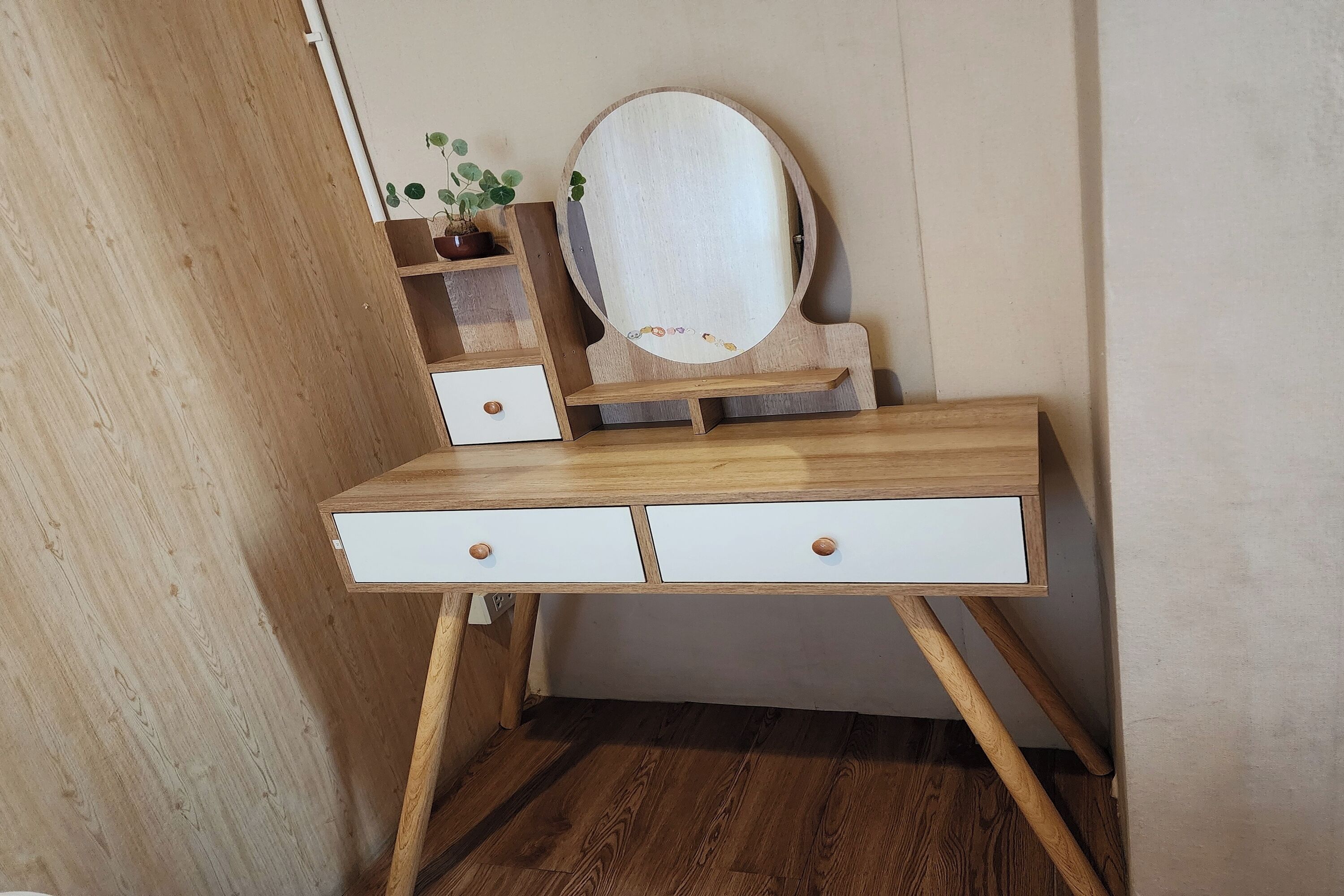 A wooden vanity with a mirror, two drawers, and a shelf with a plant.
