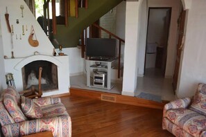 Ein Wohnzimmer mit gestreiften Sofas, einem Kamin, einem Fernseher auf einem Schrank und einer Treppe.