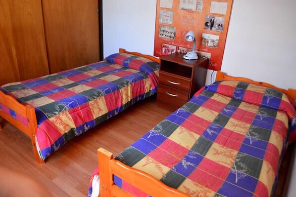 Dos camas individuales con colchas coloridas, un armario de madera y un pequeño escritorio con una lámpara.