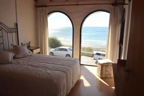 Un dormitorio con una cama grande, dos ventanas con cortinas y vistas al mar, además de un coche afuera.